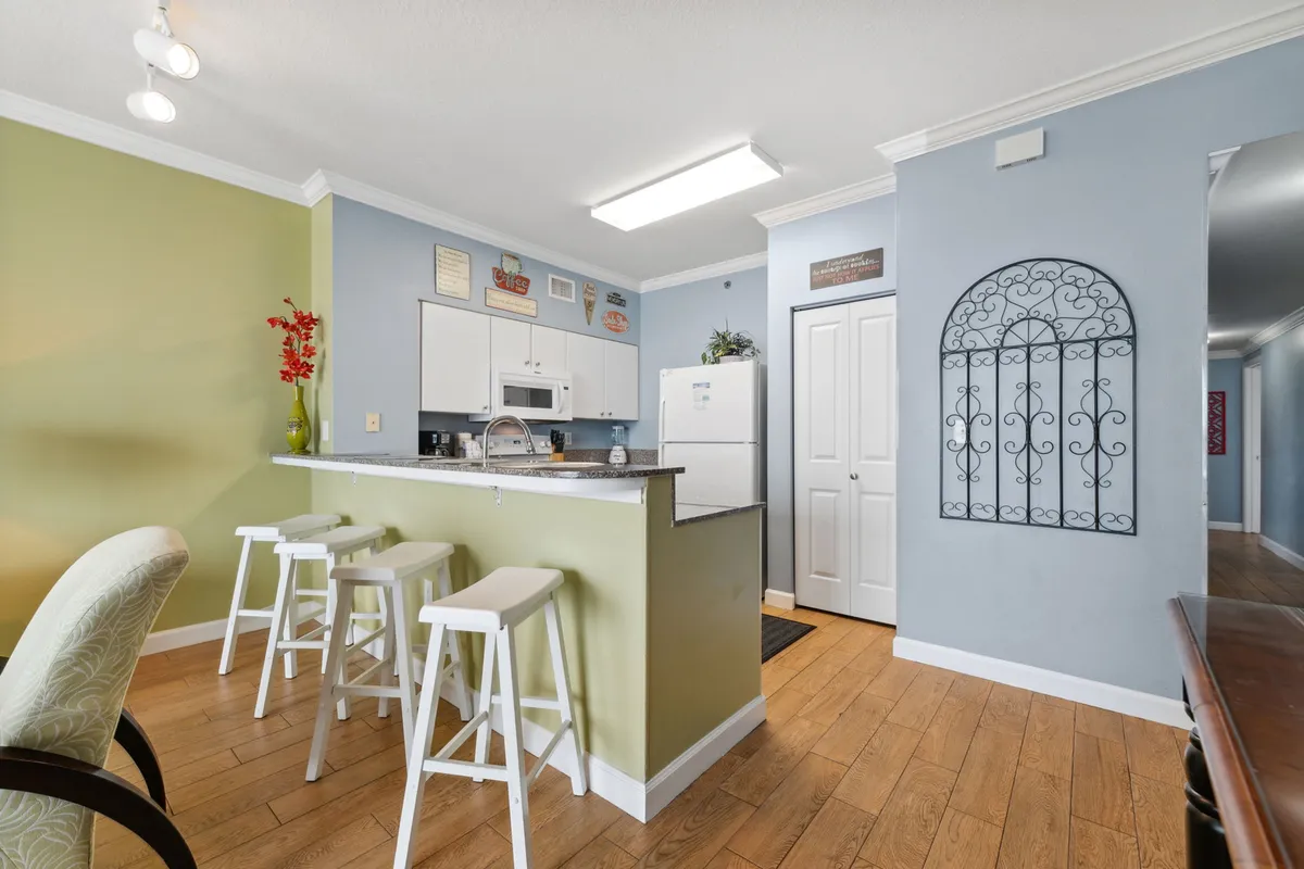 This image features a bright kitchen with a central island, white cabinetry, and decorative wall art set against a cheerful green accent wall. The countertops offer ample workspace, and the kitchen is clearly set up for both cooking and entertaining, with seating available at the island and an inviting, open layout.
