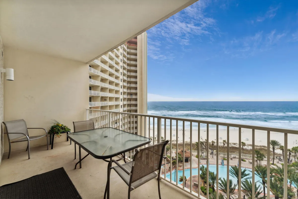 An elevated perspective from the balcony, showing comfortable balcony furniture overlooking a sparkling swimming pool below and the vast ocean beyond. The inviting outdoor setting is perfect for soaking in the sun, sharing a meal, or enjoying the sound of waves.