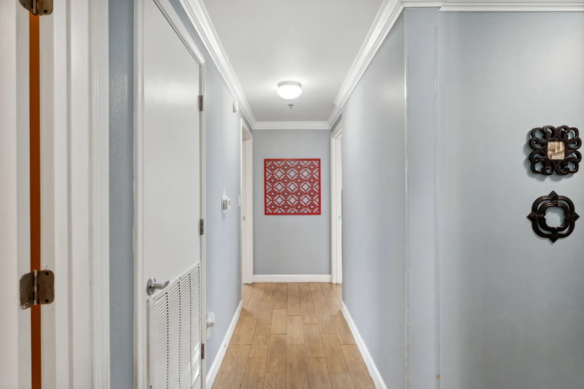 This interior hallway features wood-tone ceramic flooring, red framed artwork at the end, and white doors lining either side. Decorative wall hangings add a touch of personality and warmth. The space feels quiet, functional, and subtly welcoming, serving as a transition area within the home.