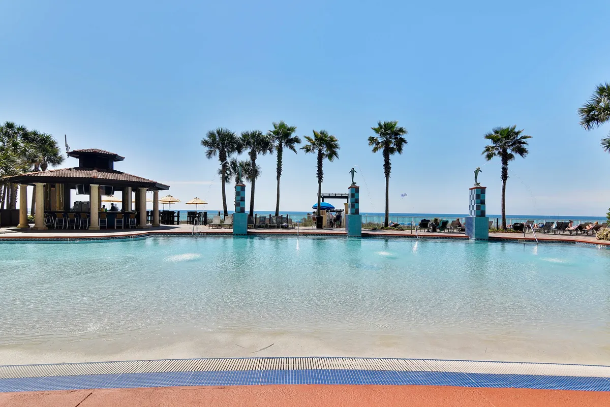 The scene showcases a large lagoon-style swimming pool with fountains, a poolside tiki bar pavilion, a row of palm trees, and the ocean horizon visible beyond the pool area. Guests are shown swimming, lounging, and socializing, all within a setting that radiates a calm, tropical vacation vibe.