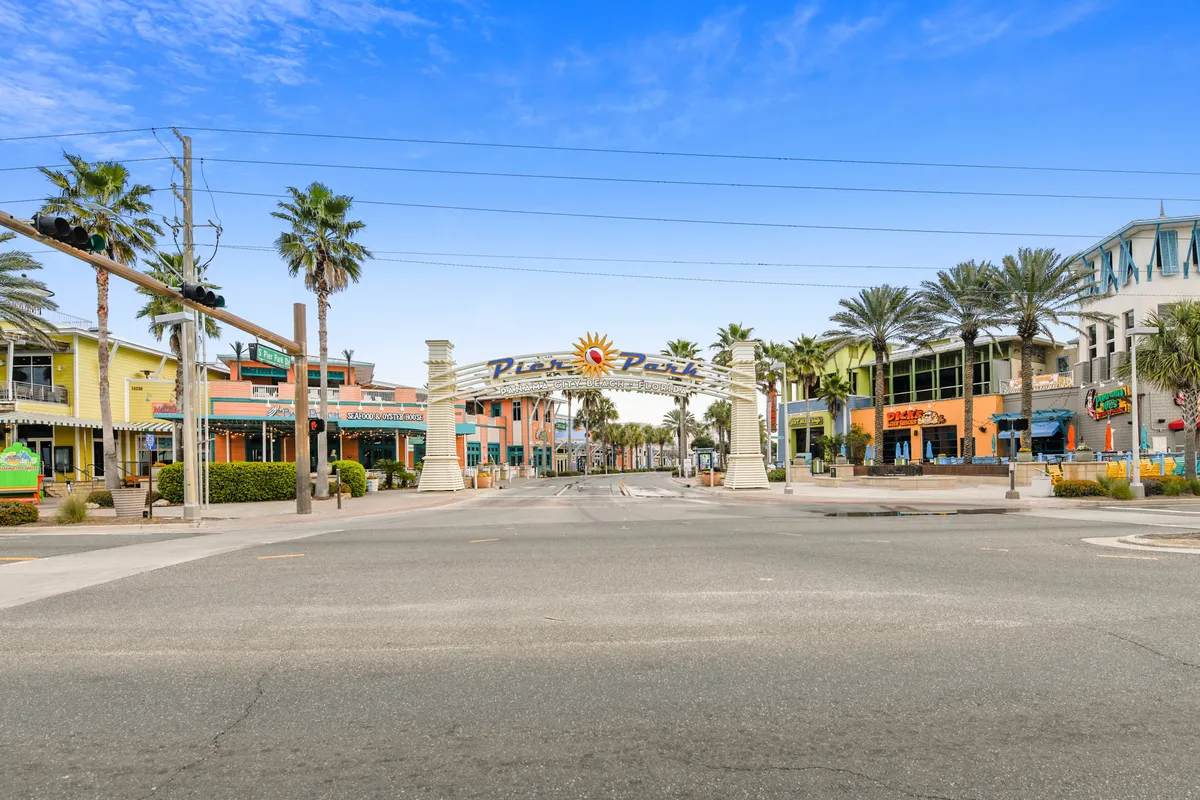 An energetic exterior shot of the Pier Park entrance archway, lined with palm trees and colorful storefronts. The wide street welcomes visitors into the heart of Panama City Beach’s shopping, dining, and nightlife district, bustling with activity and coastal charm.